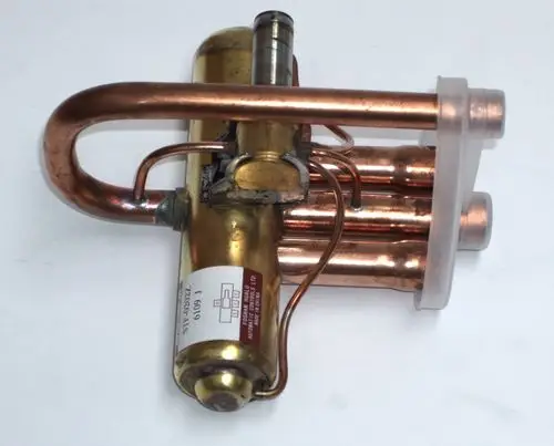 Daikin 4-Wege-Ventilkörper aus Kupfer mit mehreren Rohren und einem goldfarbenen Element. Sichtbarer Aufkleber mit Modellnummer und Seriennummer.